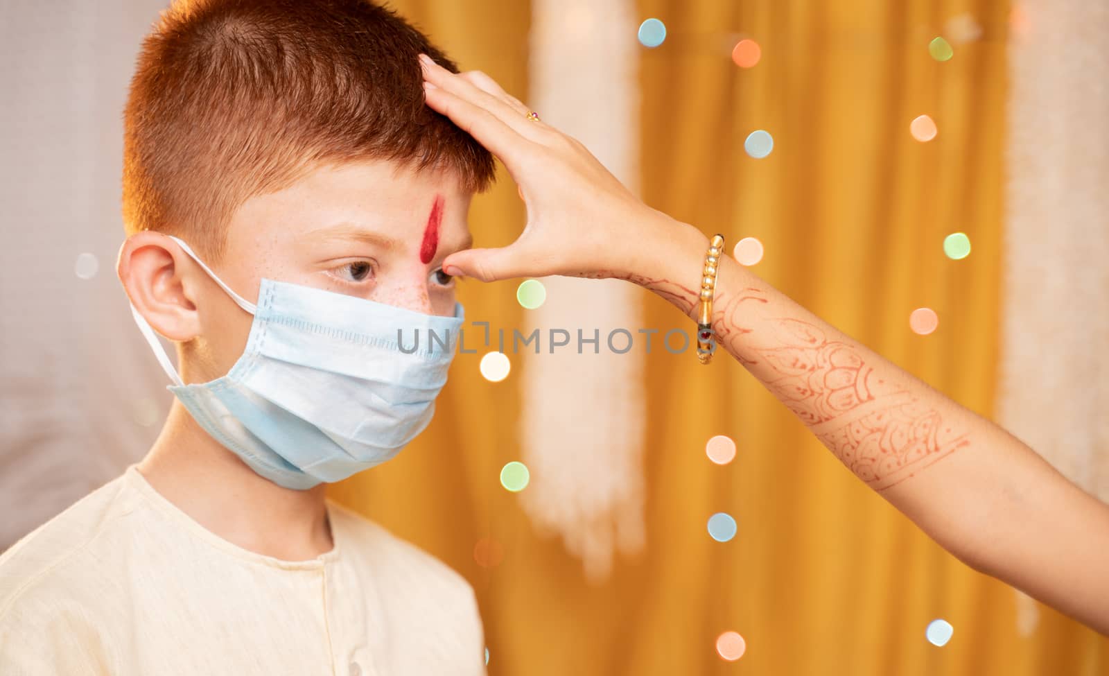 Close up Hands of Sister applying Tilaka or mark to forehead of Brother with medical mask during Bhai Dooj or Bhaubeej Indian religious festival.