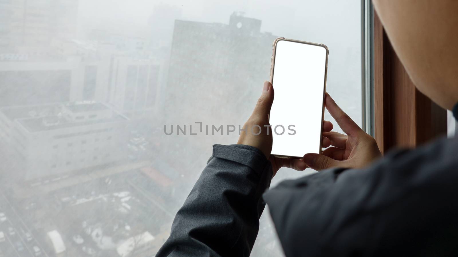Woman hand holding mobile phone with blank white screen mockup near window at outside a snowy.