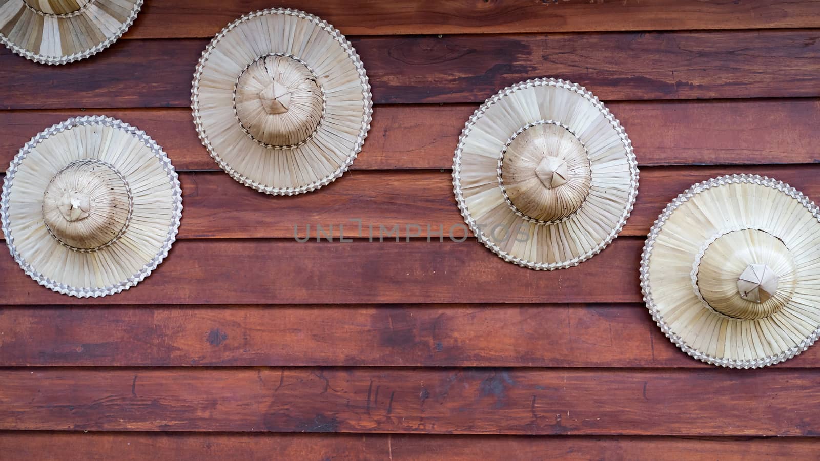 Farmer hat made of palm leaves displays decoration on wood plank wall.