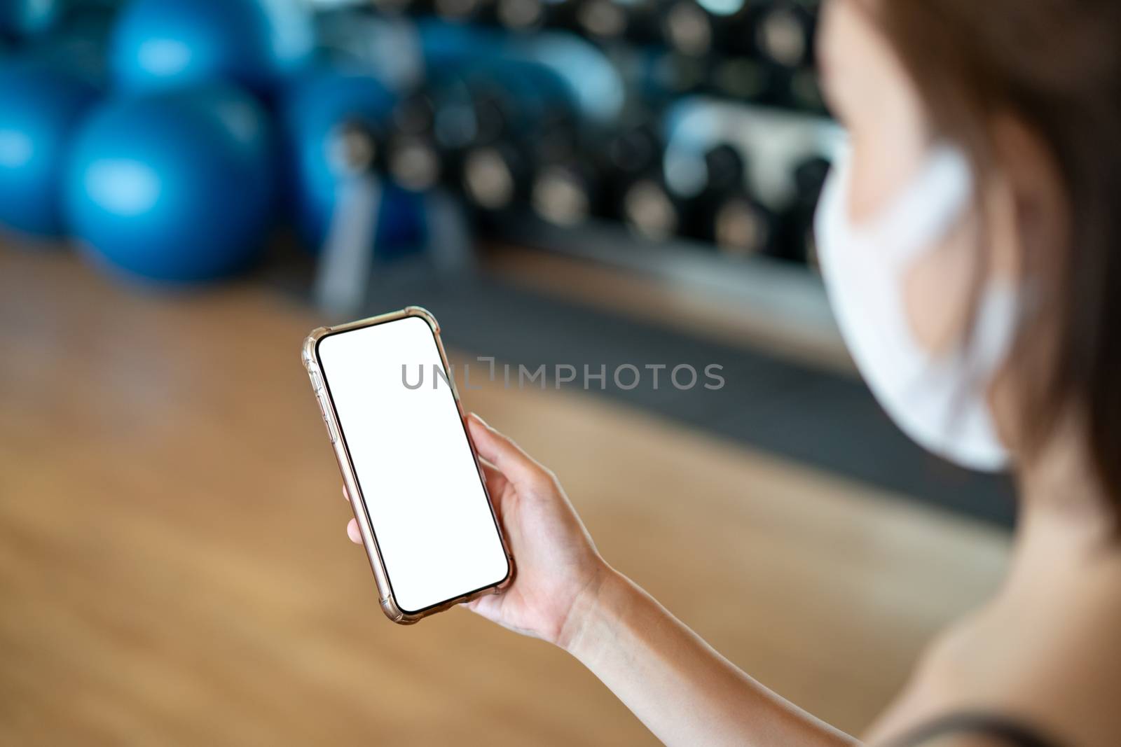 Women wearing mask making holding mockup mobile phone in the gym.