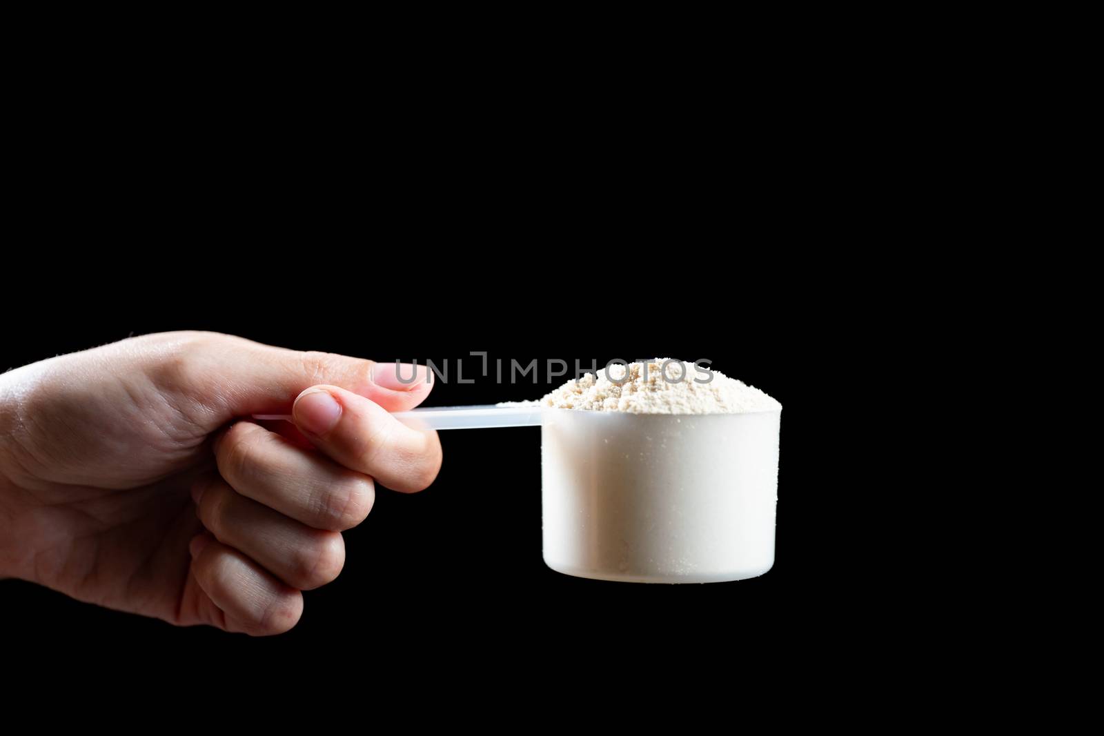 Close up of women hand holding measuring scoop of whey protein preparing protein shake.