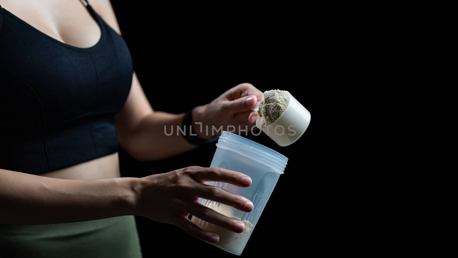 Close up of women with measuring scoop of whey protein and shaker bottle, preparing protein shake.