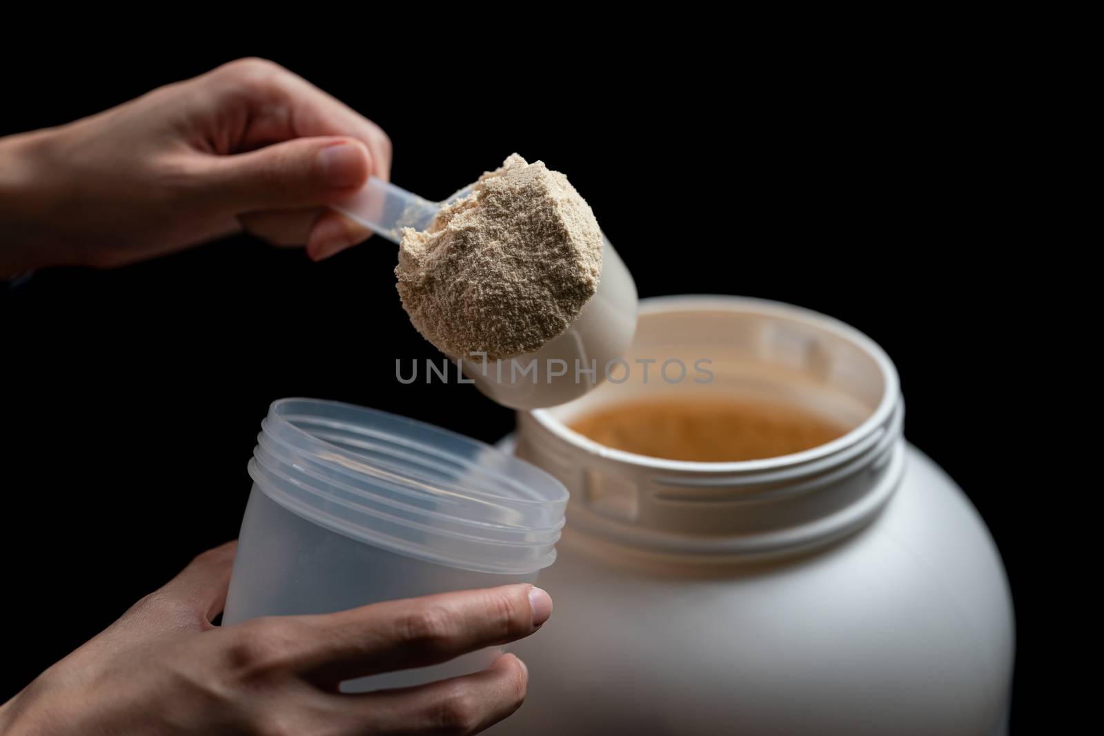 Close up of women with measuring scoop of whey protein, jar and shaker bottle, preparing protein shake.