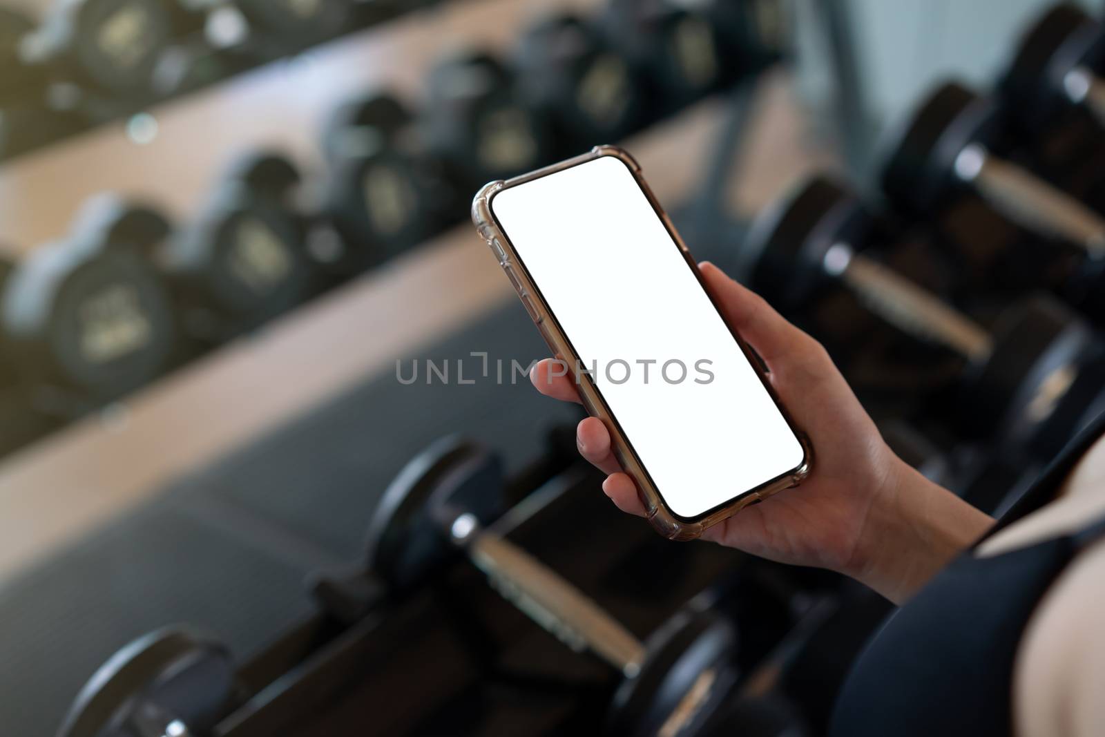 Woman hand holding mobile phone with blank white screen mockup in gym.