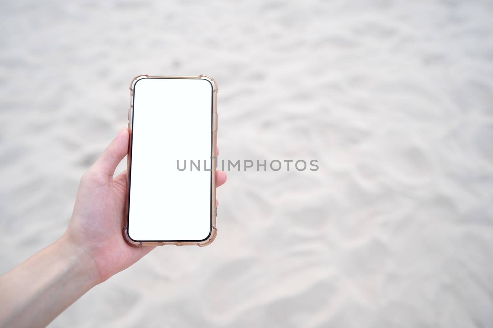 Woman hand holding mobile phone with blank white screen mockup on the beach.