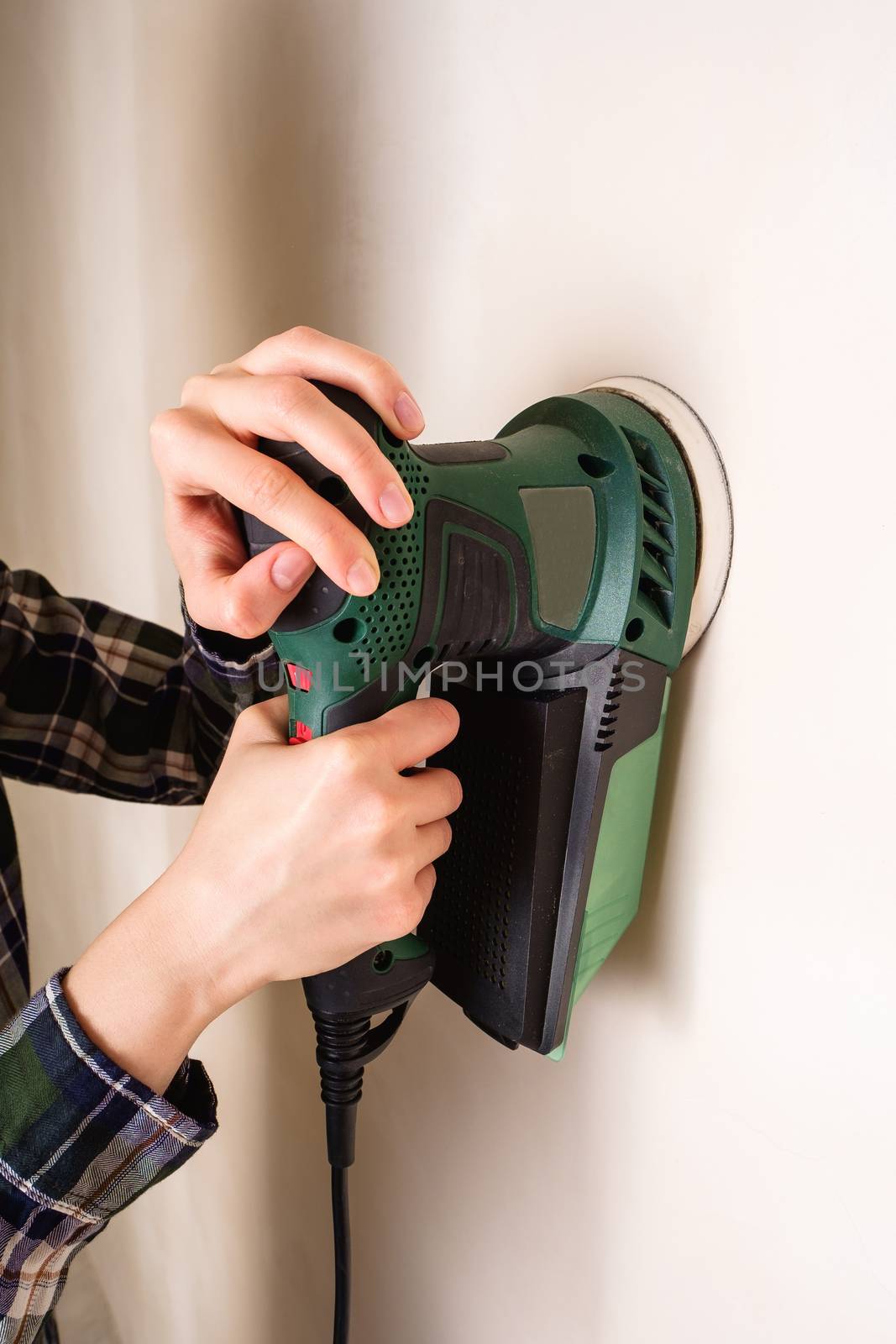 Woman hands holding and working with electric sander to smooth plaster wall surface, room renovation concept