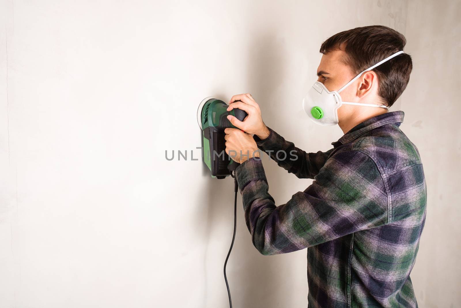 Man in protective mask working with electric sander to smooth wall by Frostroomhead