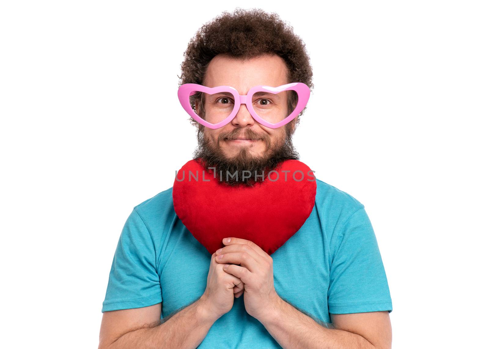 Happy Valentines Day. Crazy bearded Man with funny Curly Hair in heart shaped eye Glasses. Happy and silly guy in Love, isolated on white background. Portrait of Cheerful man with Red plush Heart.