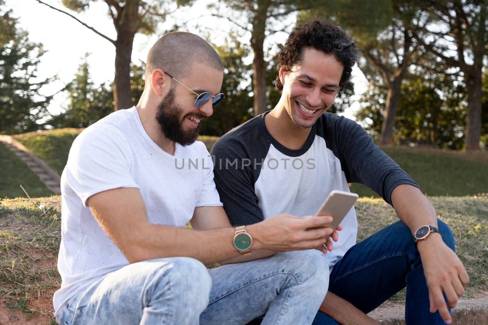 Two friends having fun with mobile in the park at sunset