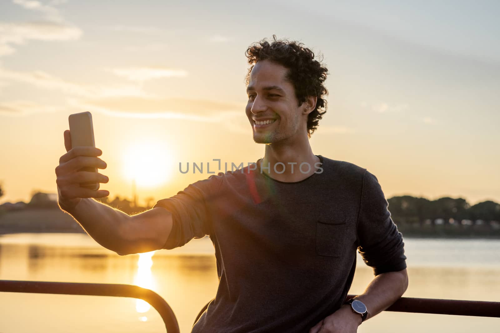 Portrait of young man using the mobile phone in the lake with beautiful sunset