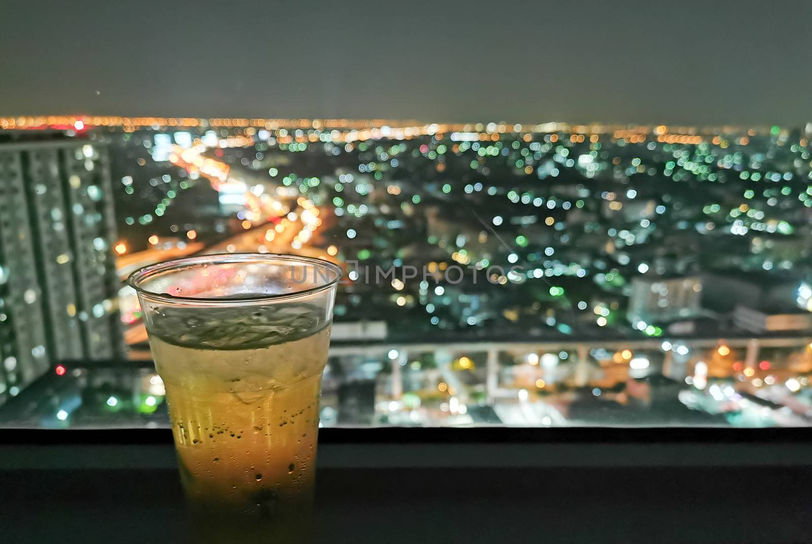 A glass of beer with cityscape from high condominium view at night.