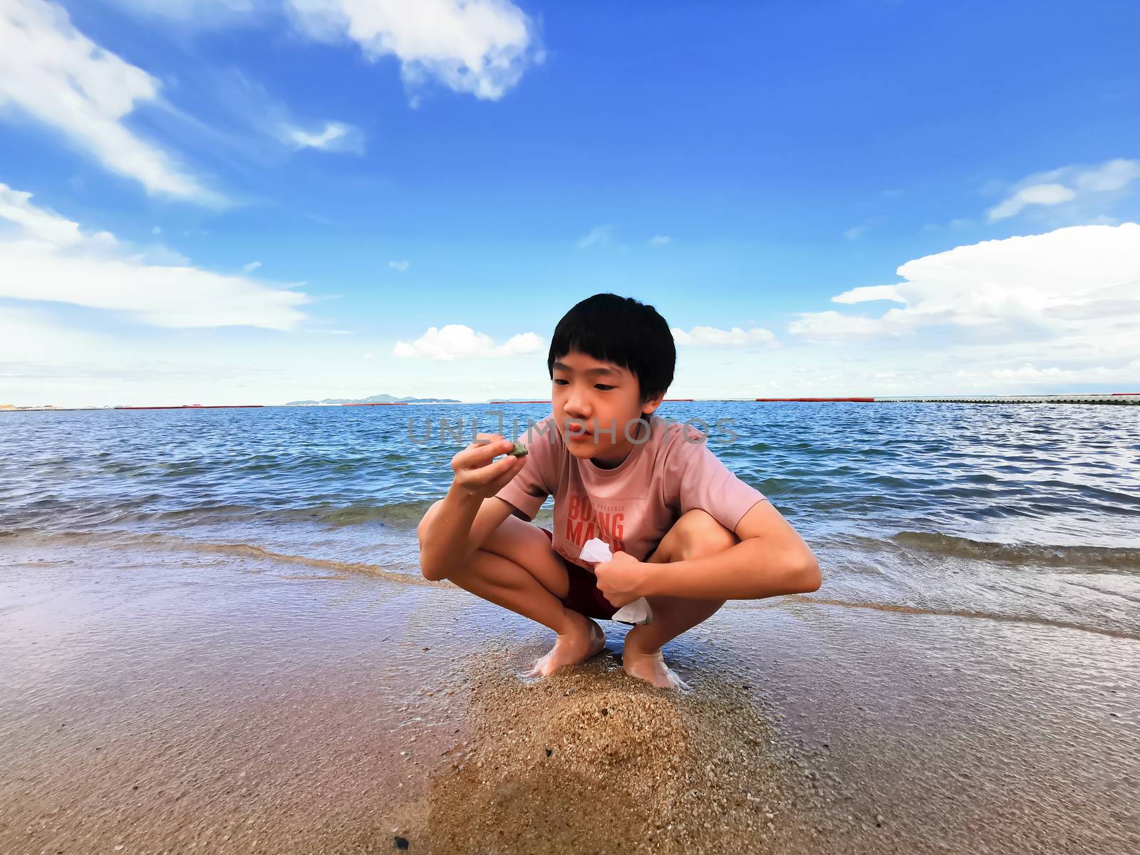 An Asian boy has playing a stone on the beach with blue sky in t by animagesdesign