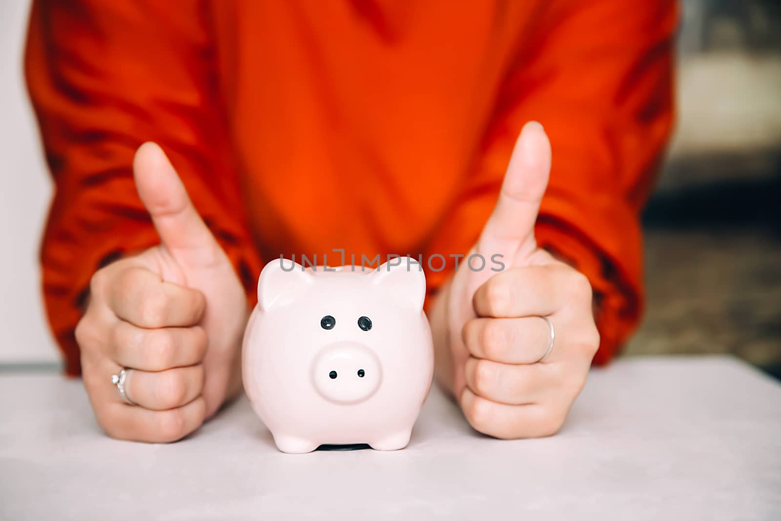 Woman in red blouse shows her thumb up all right next to pink piggy Bank