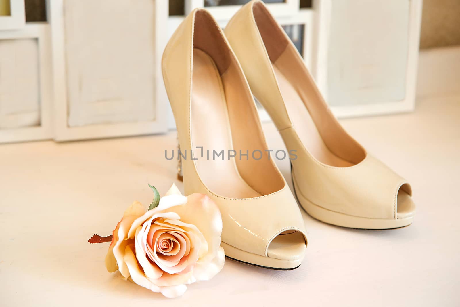 Wedding high-heeled shoes stand on a white dresser on the background of photo frames