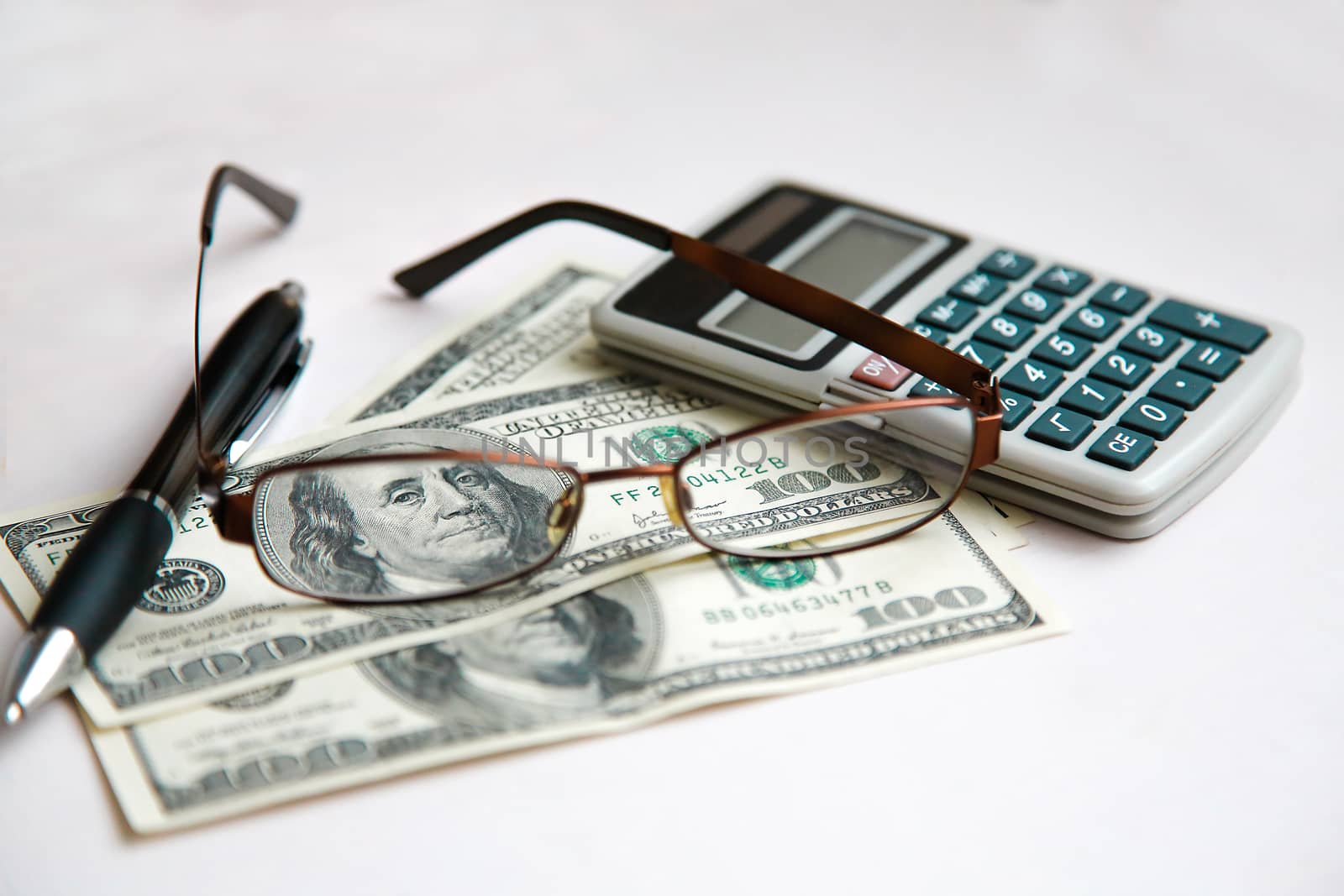 The glasses in the frame are on the dollars with the calculator on the white table.Texture.Background.