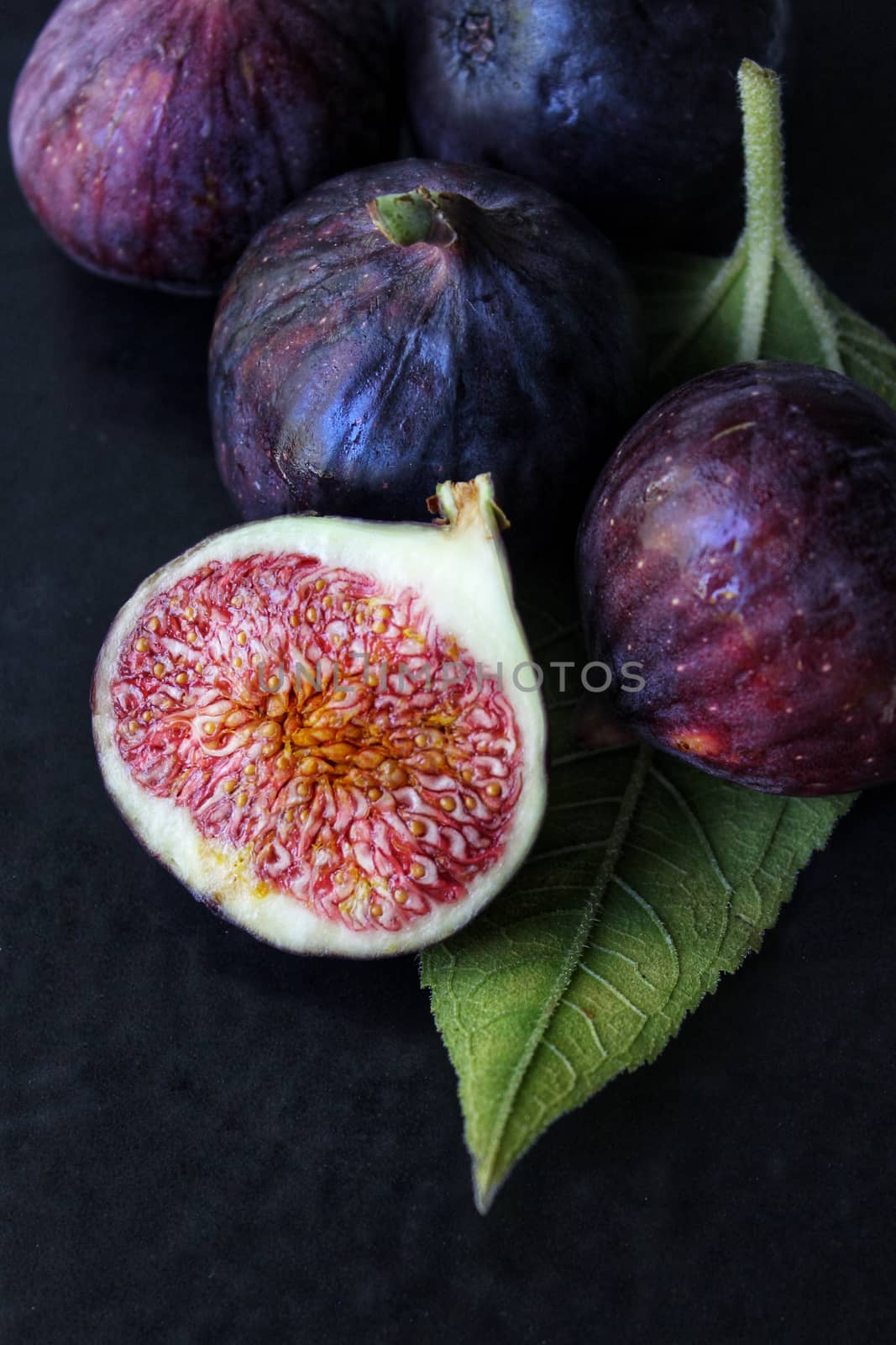 A slice of purple Fig with a green leaf on a dark background close-up by Mastak80