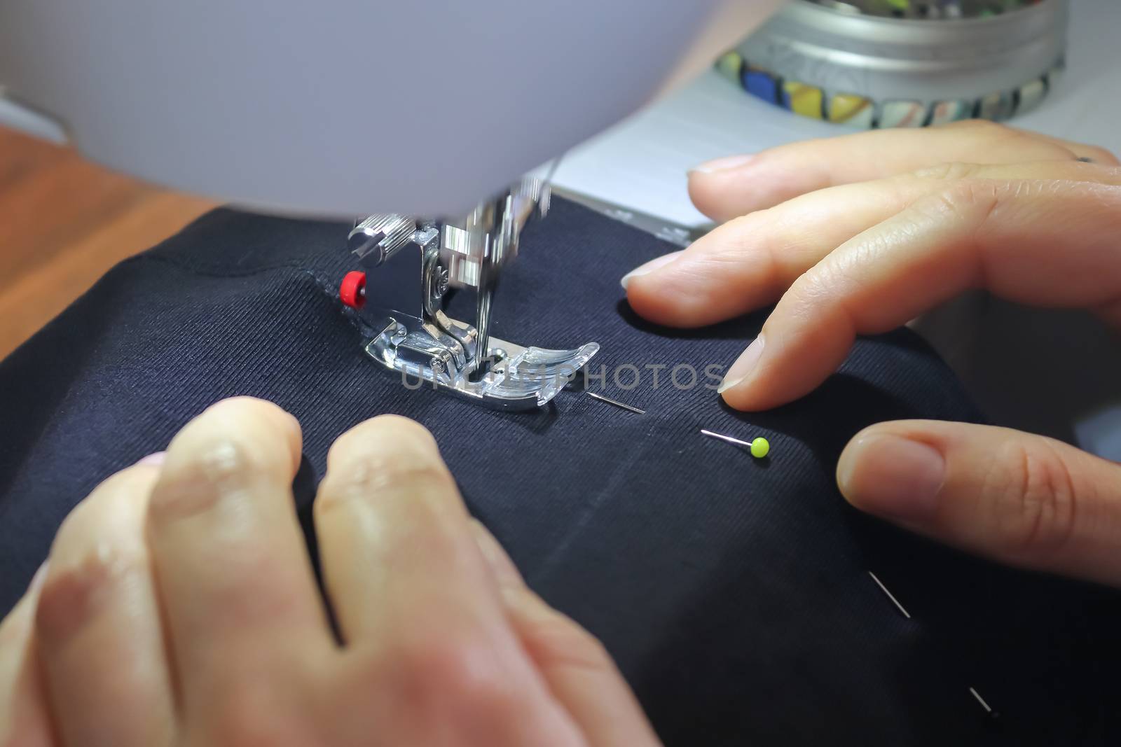 Female hands working at a modern sewing machine with some fabrics and textiles