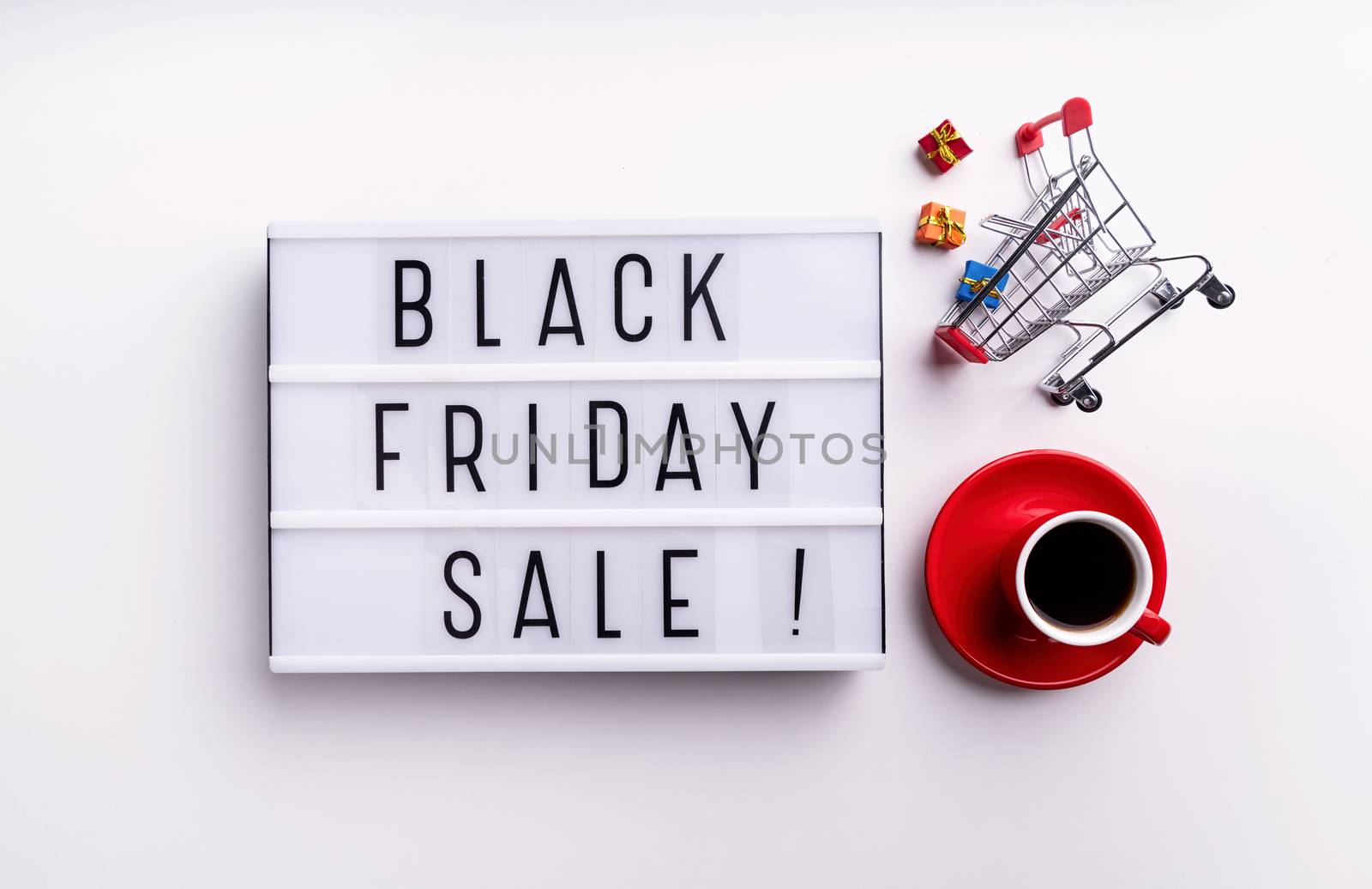 Black Friday shopping sale concept. Black Friday Sale words on lightbox with cup of coffee and shopping cart top view flat lay on white background