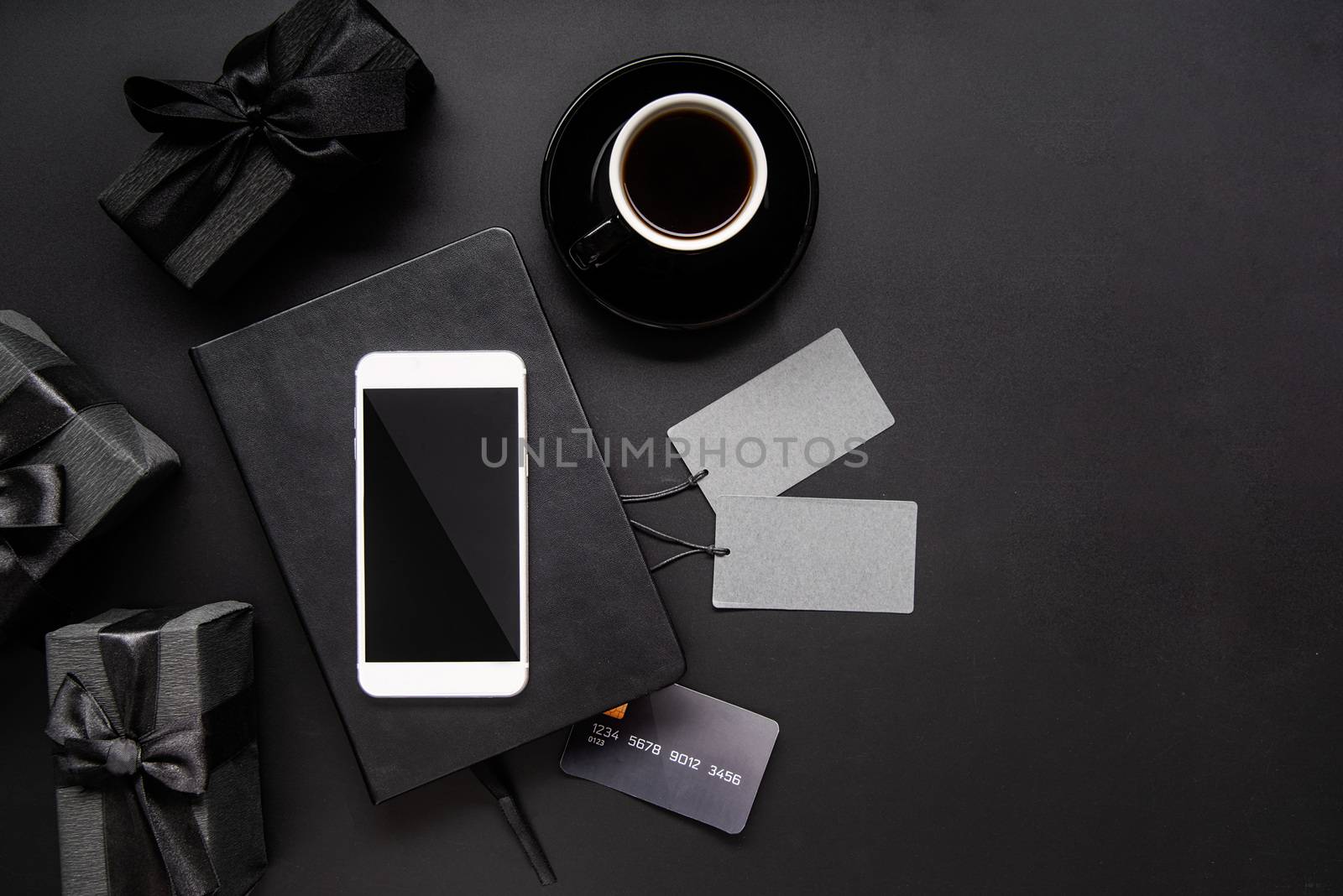 Black Friday shopping sale concept. Black smartphone, price tags, coffee and gifts top view flat lay on black background with copy space