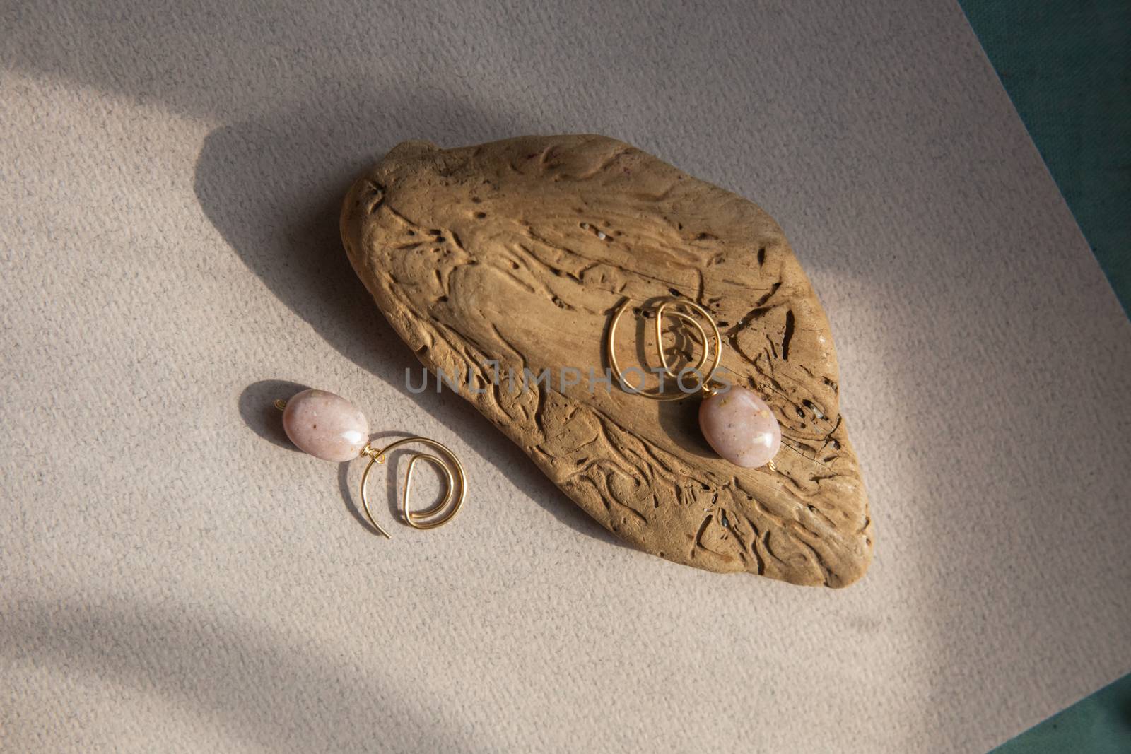 Stylish earrings made of natural pink opal stone with Golden brass fittings on piece of wood pattern from the activity of bark beetle. Natural day solar lighting.
