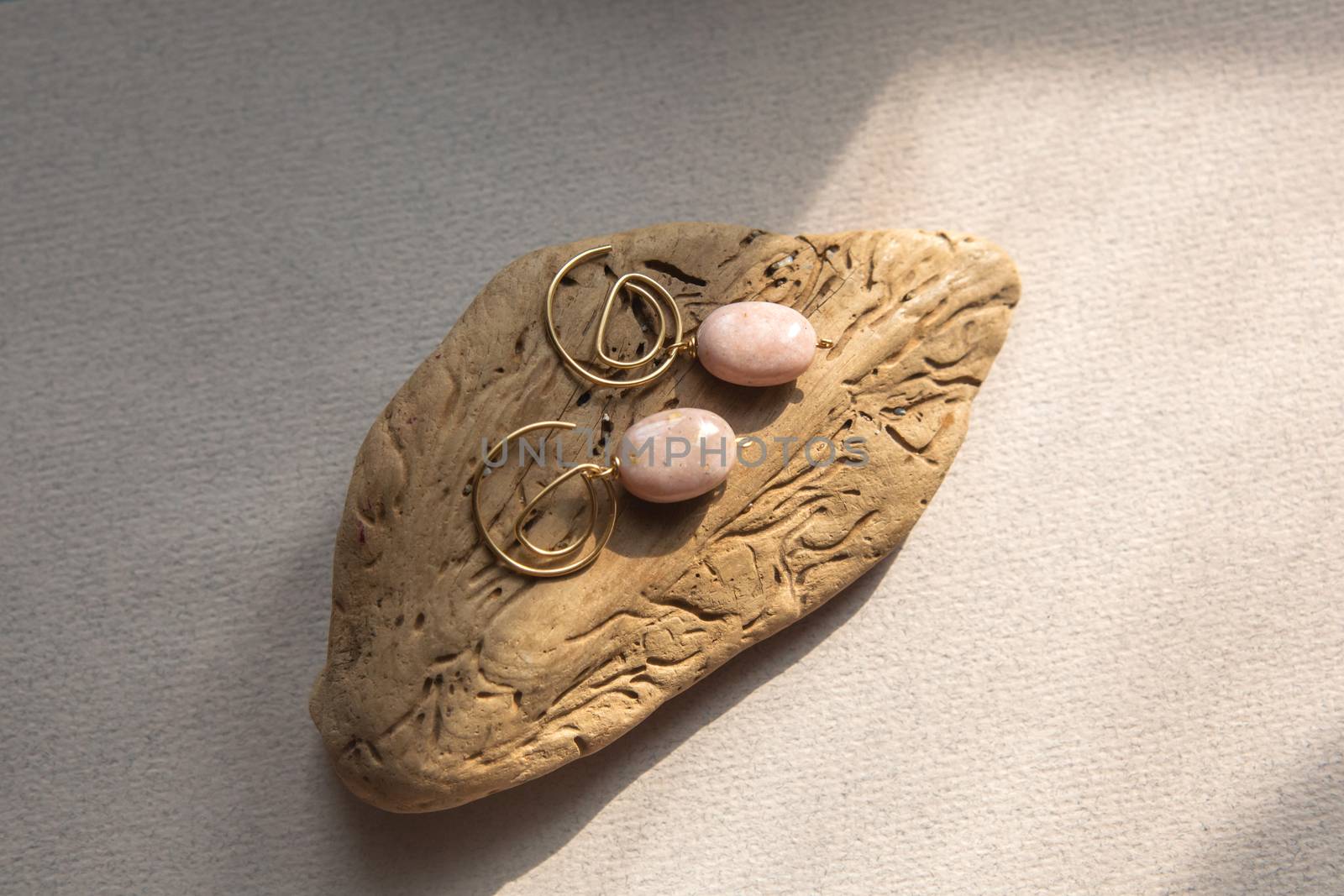 Stylish earrings made natural pink opal stone with Golden brass fittings piece of wood pattern from activity bark beetle. Natural day solar lighting.