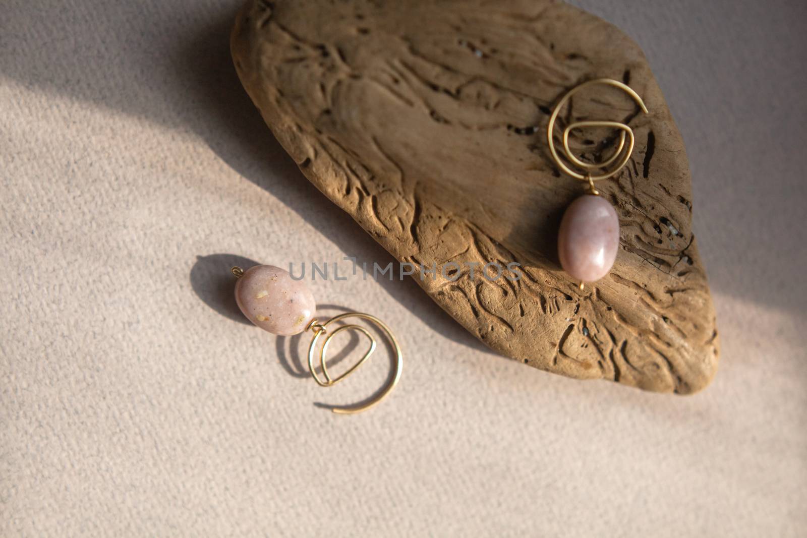 Stylish earrings made natural pink opal stone with Golden brass fittings piece of wood pattern from activity bark beetle. Natural day solar lighting.