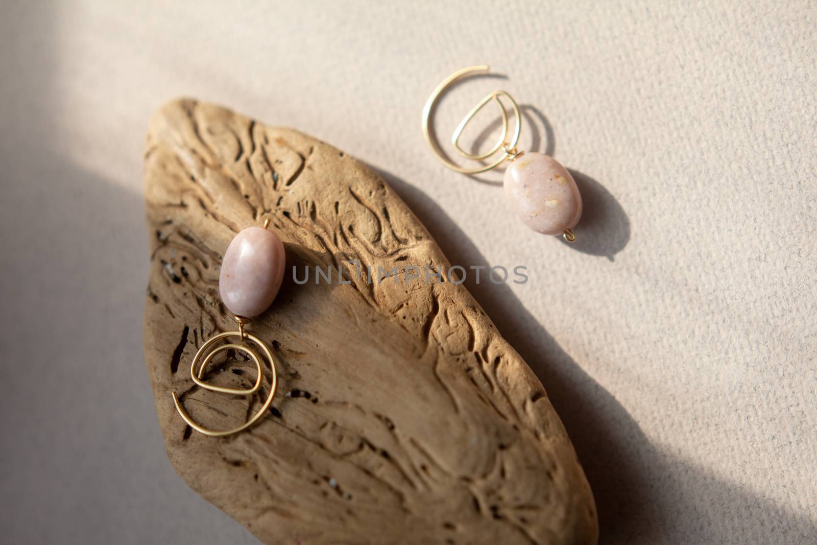 Stylish earrings made natural pink opal stone with Golden brass fittings piece of wood pattern from activity bark beetle. Natural day solar lighting.