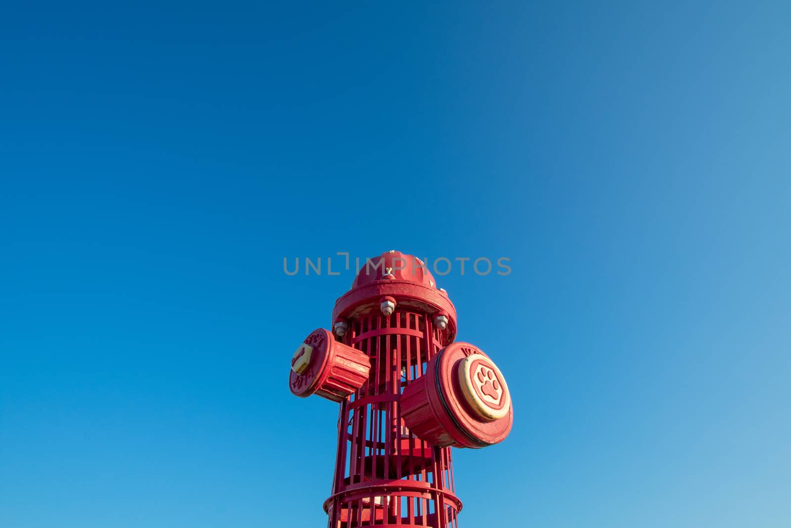 A Giant Red Fire Hydrant at a Dog Park on a Clear Sky