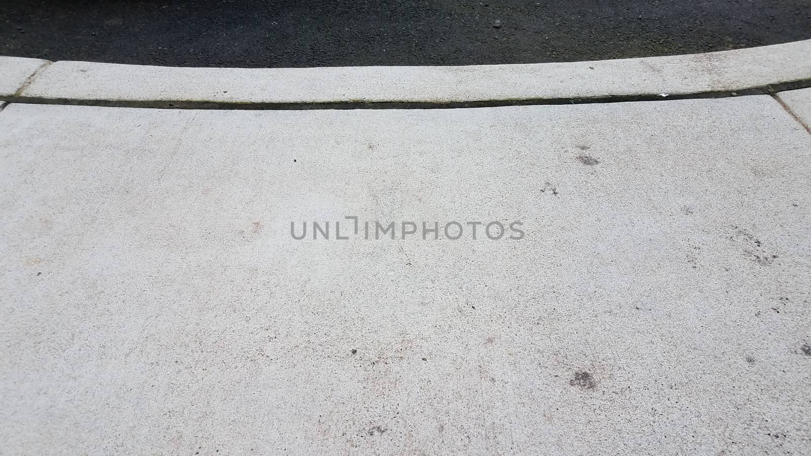 grey cement sidewalk and curb with asphalt or road
