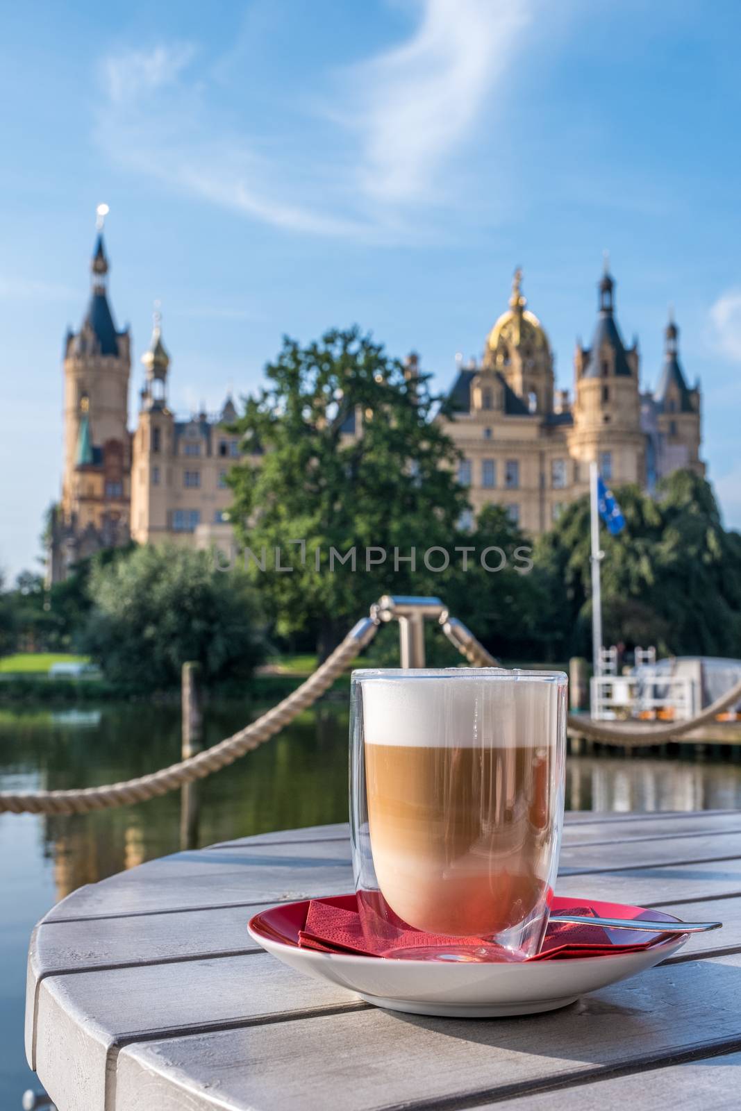 Cup of cappuccino in an outdoor cafe or restaurant on a summer day with a beautiful castle in Schwerin in the background.