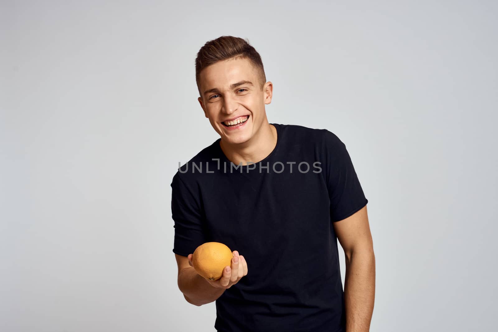 A guy with an orange in his hand and in a black T-shirt on a light background cropped view by SHOTPRIME