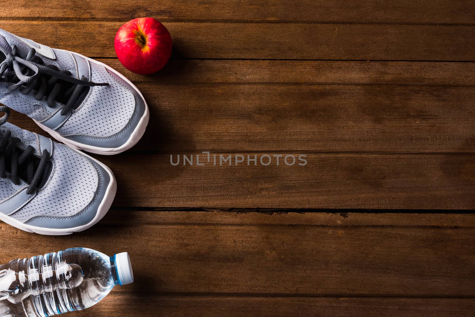 Top view of pair sports shoes, bottle water and red apple on wood table, Gray sneakers and accessories equipment in fitness GYM, Healthy workout concept