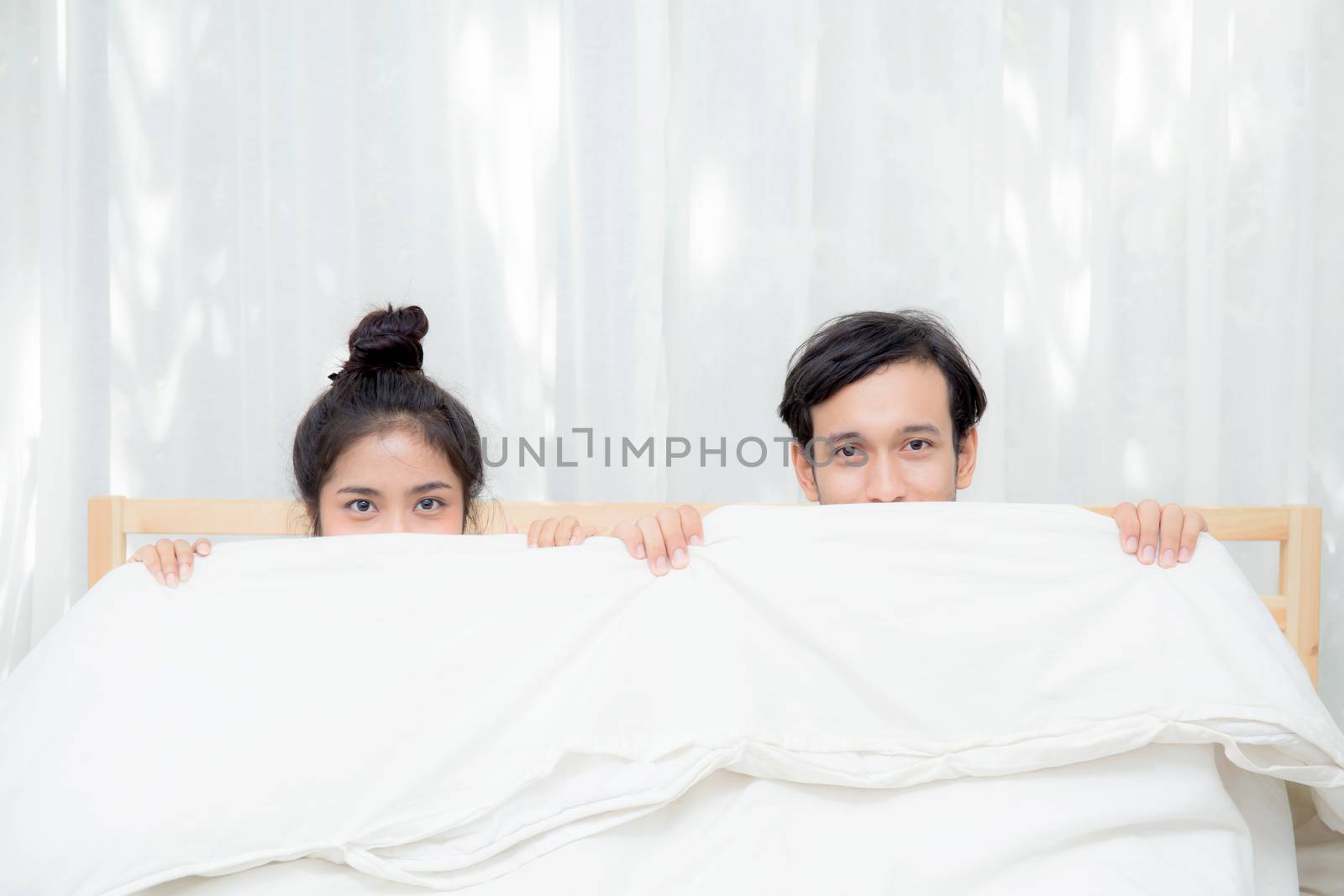 Asian young lovely couple sitting in a bed, happy smile looking at camera, cover under blanket.