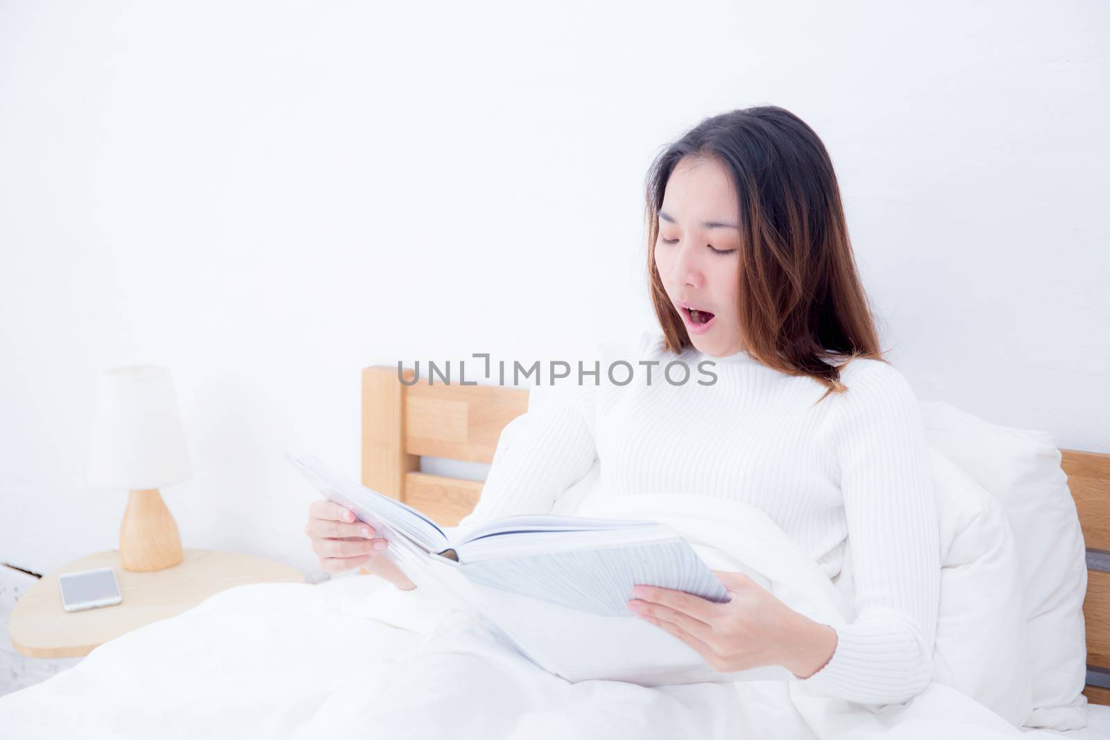 Asian woman reading a book and yawn in bedroom. lifestyle concept.