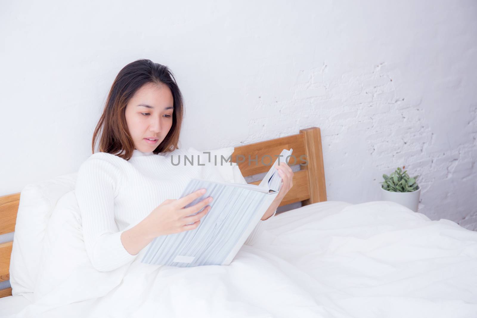 Asian woman reading a book and smiling in bedroom. lifestyle concept.
