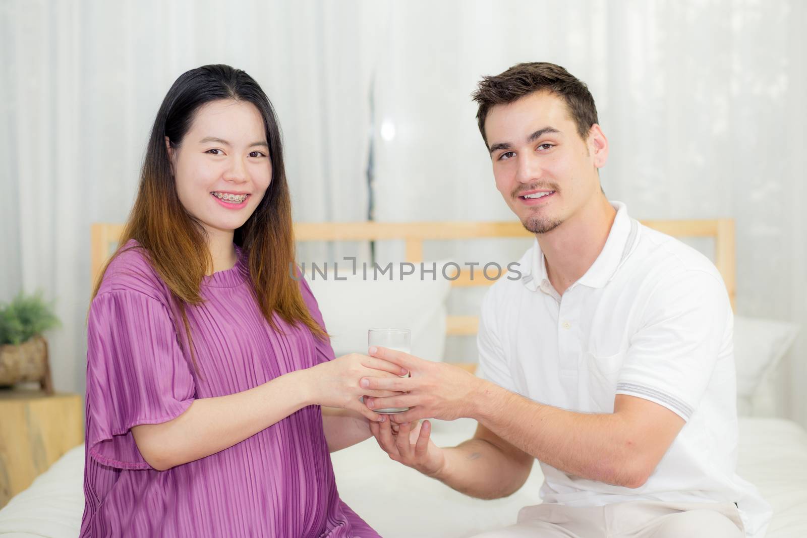 Asian handsome husband takes care about pregnant woman with gives a glass of milk lovely pregnant.
