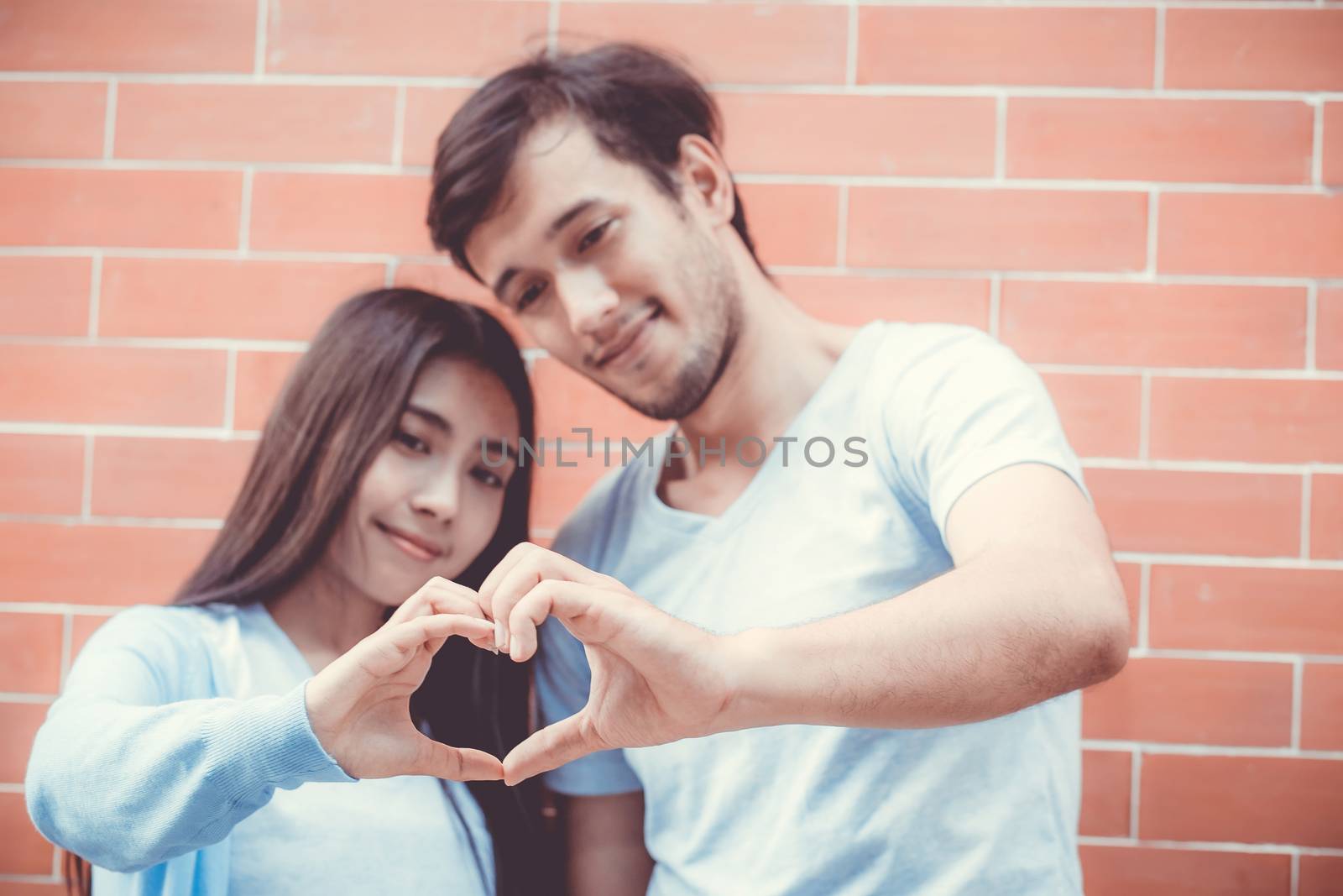 Closeup of young man and woman asian making heart shape with hand, Loving couple with heart shape of hand outdoors.