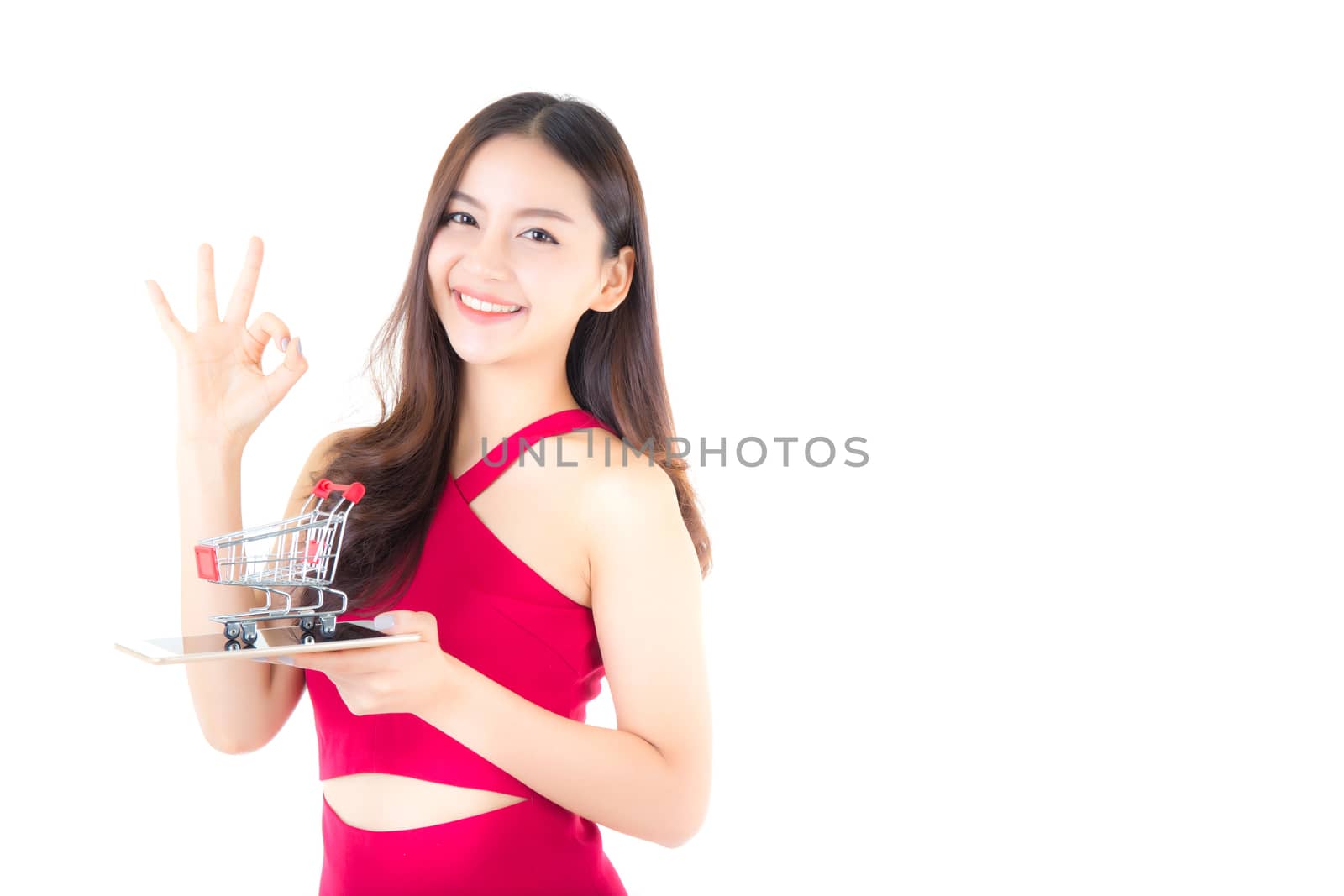 Smiling asian woman in red dress holding tablet with glad girl gesture ok and cart on tablet isolated on white background.
