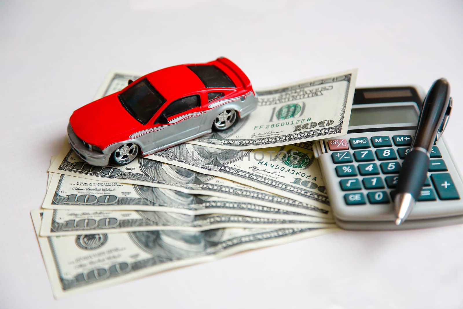The red car is on dollars spread out on a white table next to the calculator.Texture.Background.