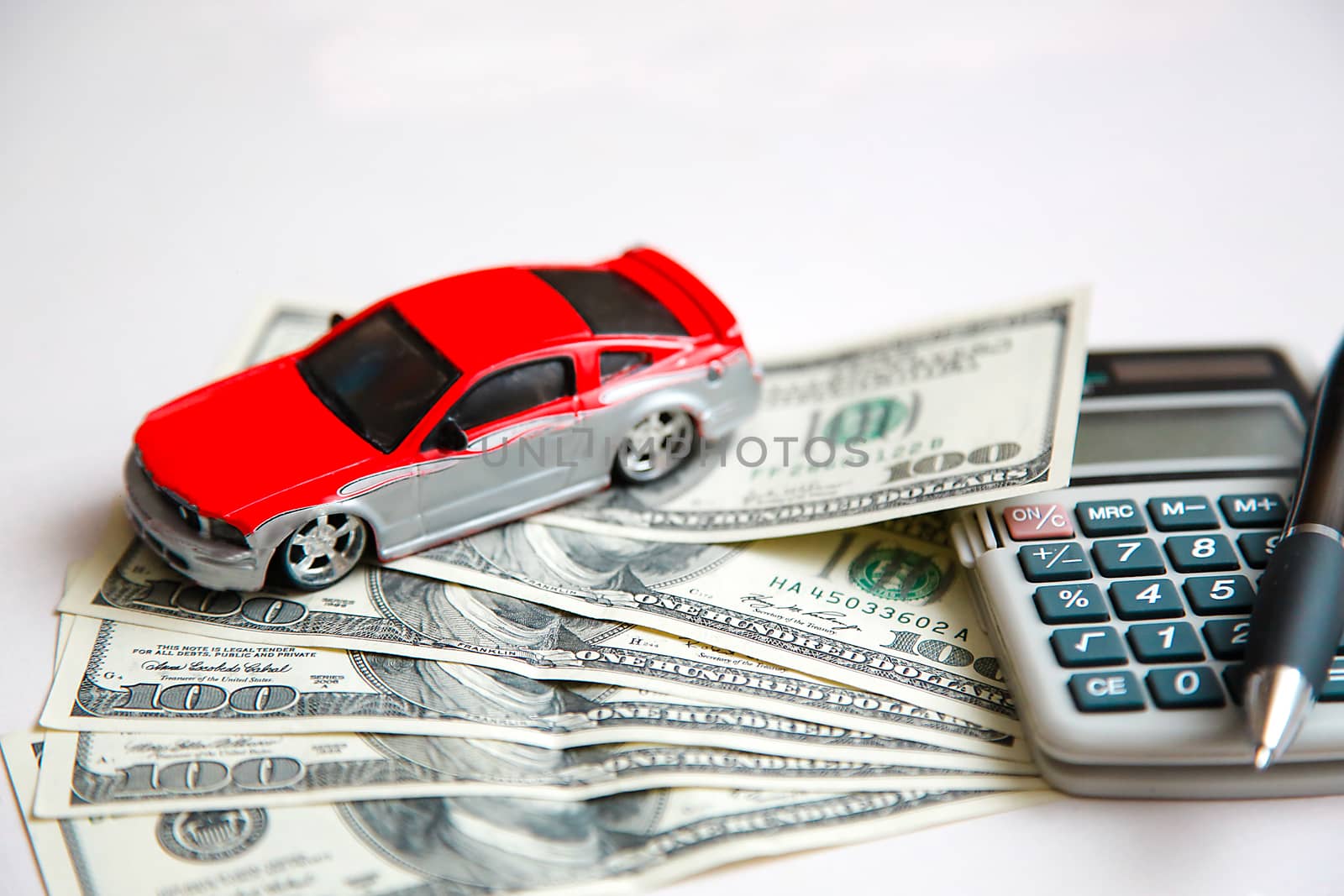 The red car is on dollars spread out on a white table next to the calculator