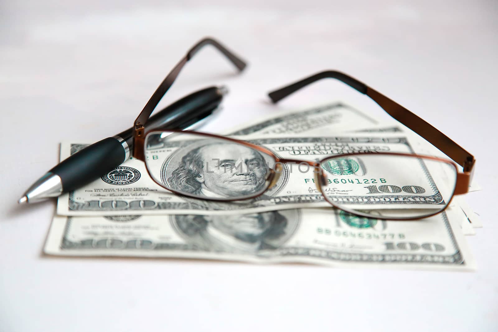 Glasses in a frame are on dollars with a black pen on a white table.Texture.Background.