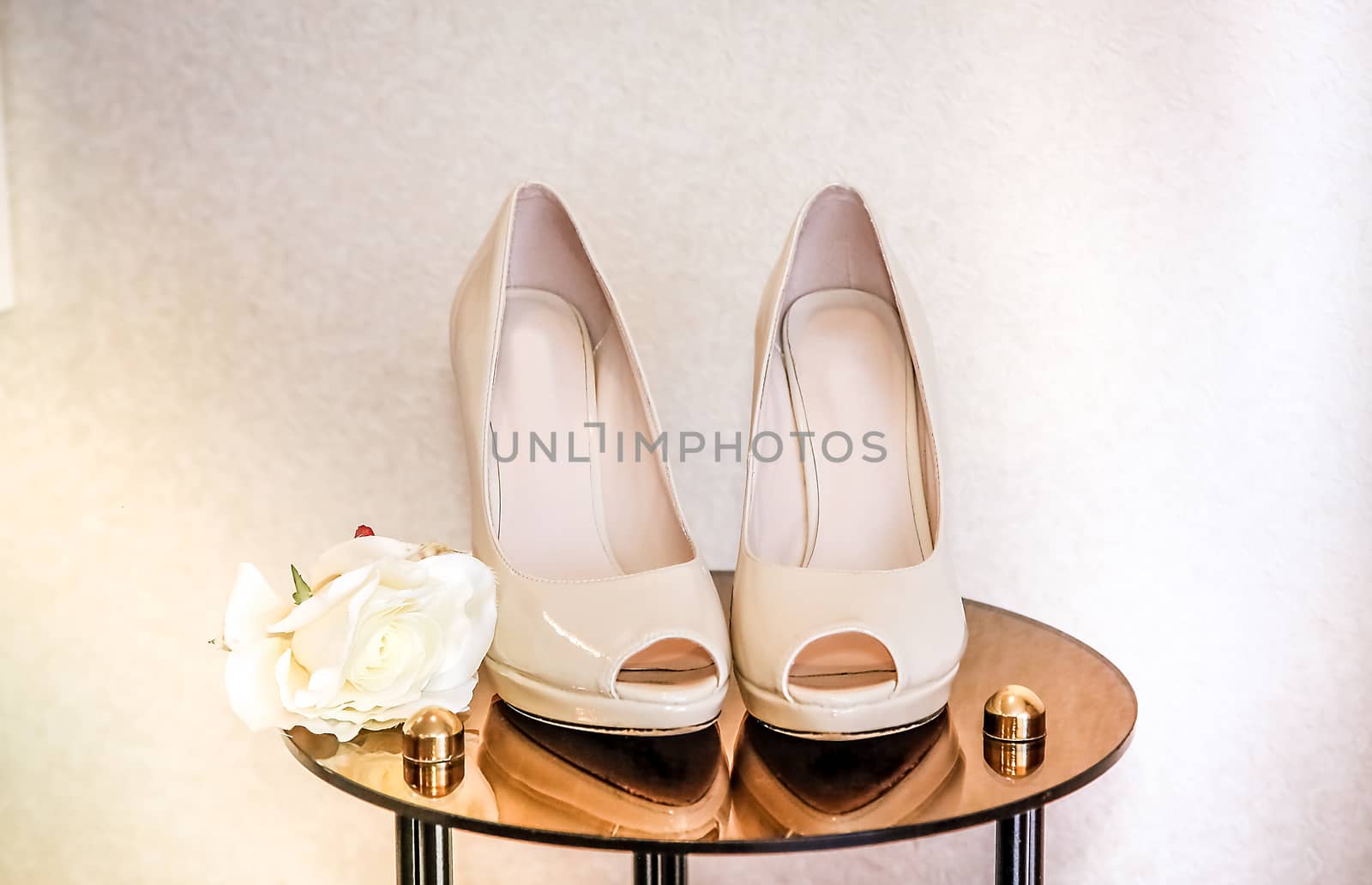 Shoes beige high-heeled stand on a mirrored table next to a rosebud