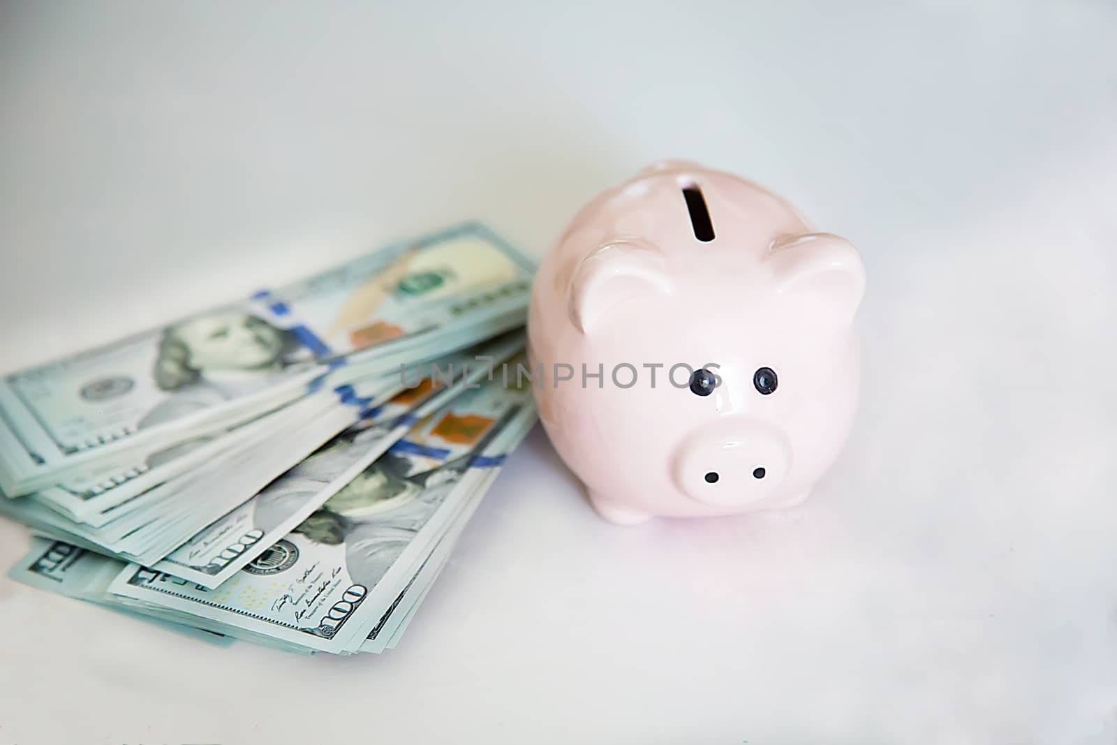 On the white table near the hundred dollar bills is a ceramic toy piggy Bank