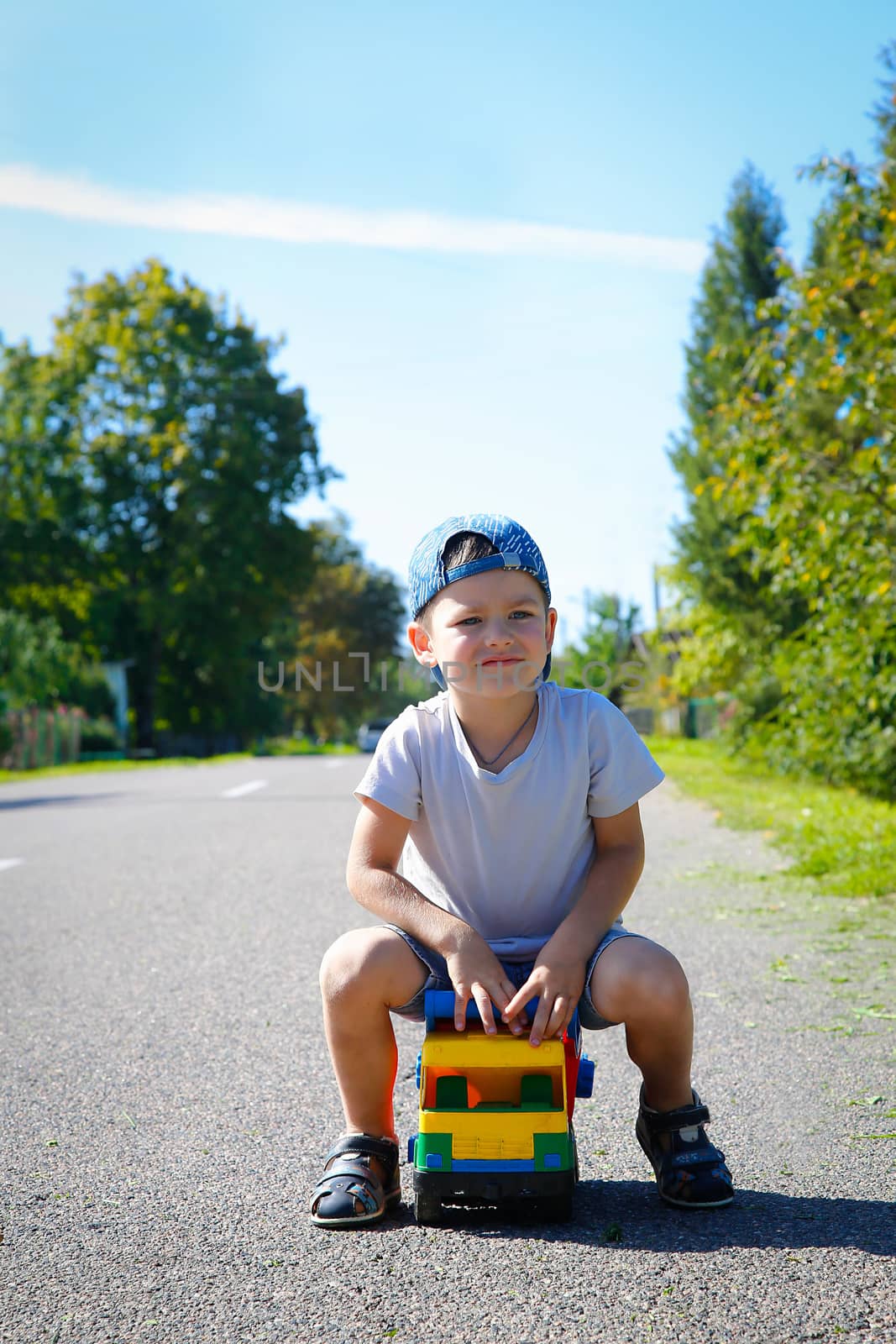 Preschool boy in summer playing alone on the road with a big truck