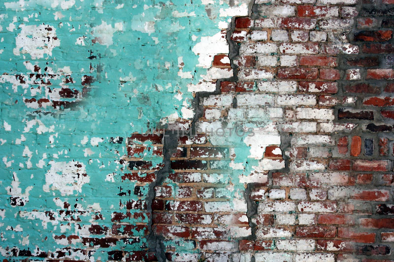 The old cracked wall is made of red brick and smeared with green and white paint