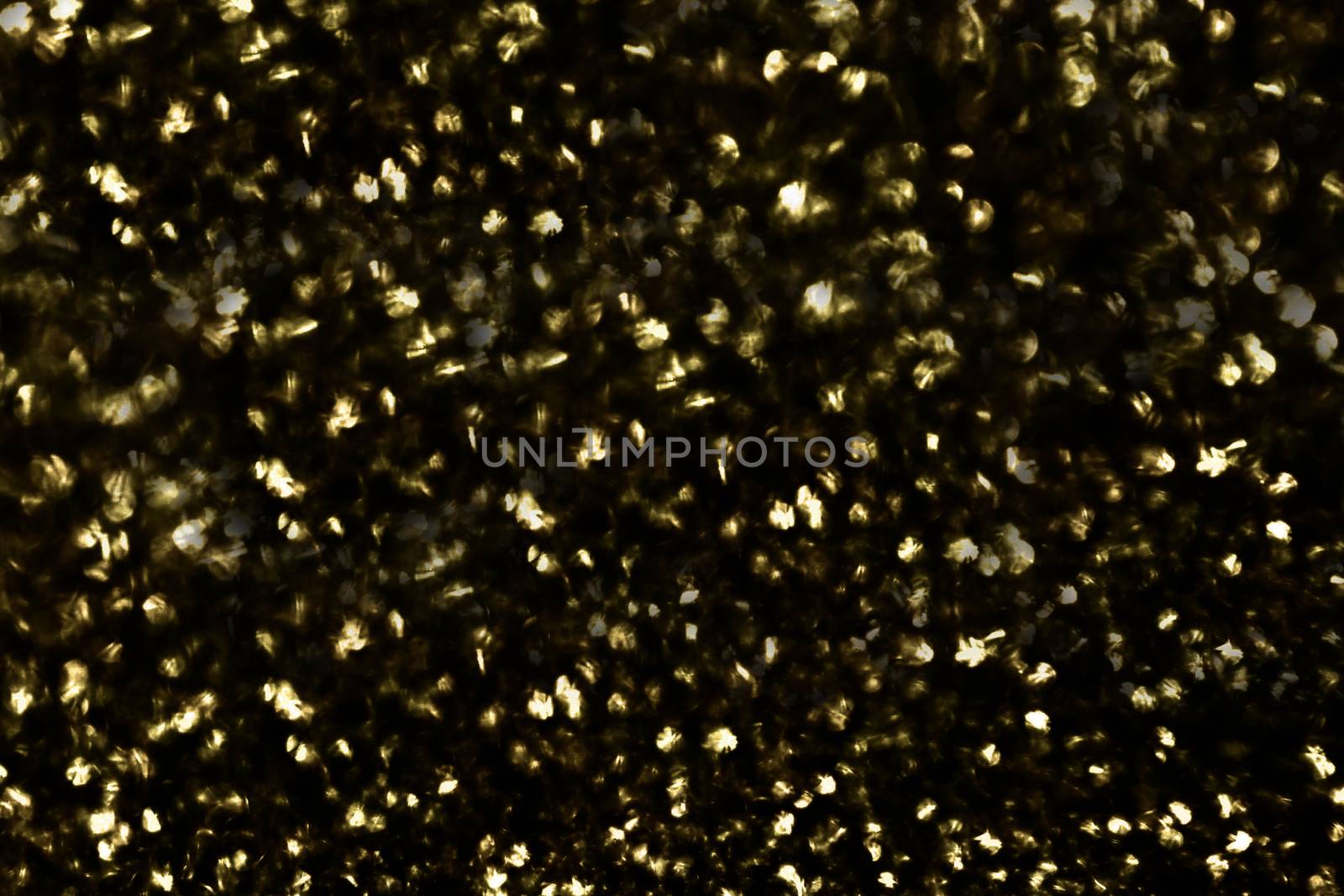 On the surface a large number of defocused round shiny gold sequins on a black background.Texture or background