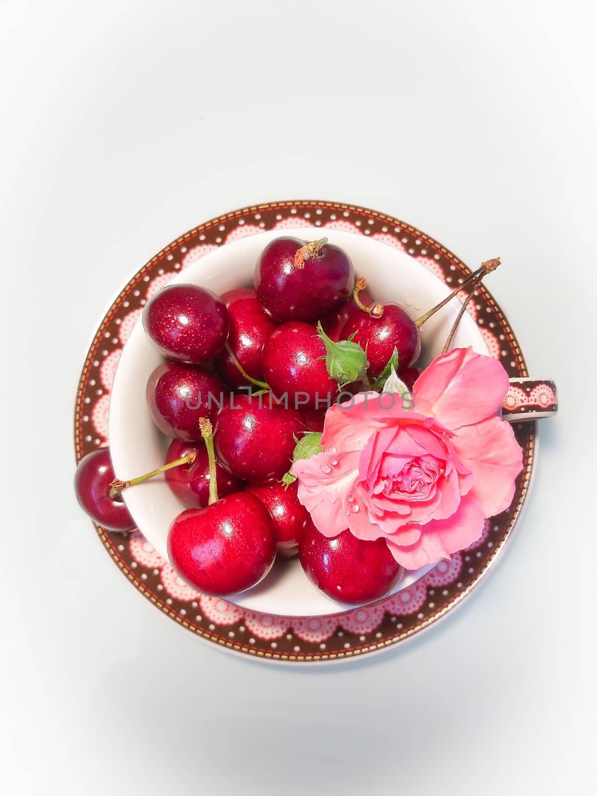 Ripe cherry with a rose flower in a ceramic plate with patterns on a white background