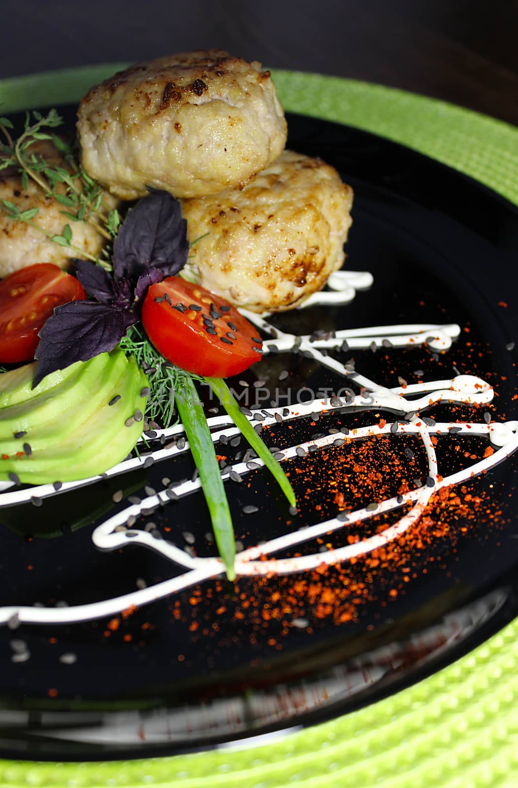 On a black plate cutlets with sliced zucchini and cherry tomatoes