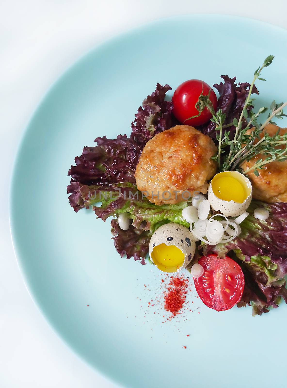 A dish with fried cutlets and quail eggs and garnished with greens and cherry tomatoes