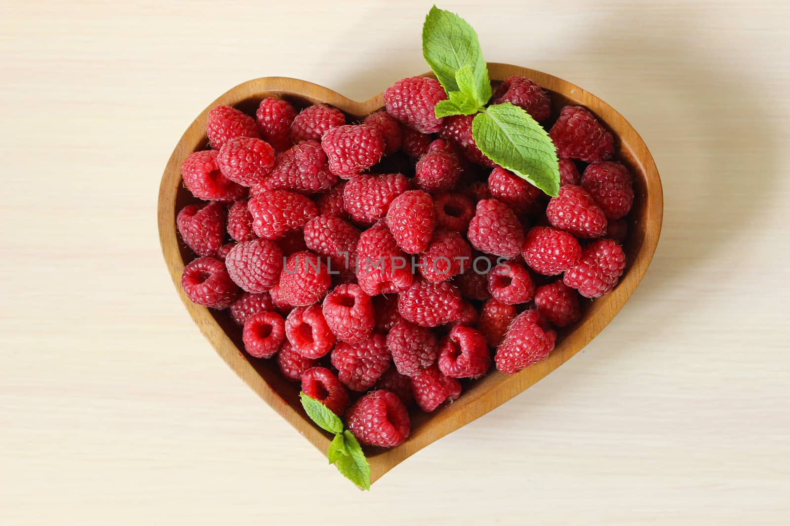 Large crop of raspberries in a wooden container on a white background